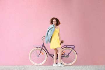 Beautiful young woman with bicycle on color wall background