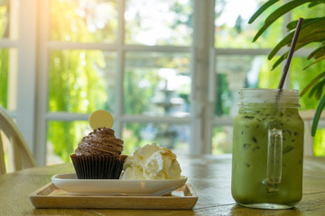 Ice green tea latte and chocolate cupcake with whipped cream frosting calories on wooden table, relax concept.