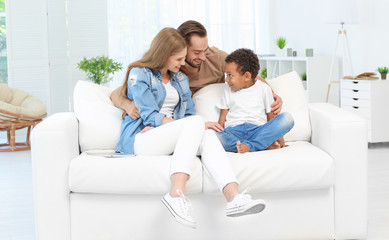 Obraz premium Happy couple with adopted African-American boy sitting on couch at home