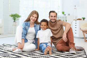 Happy couple with adopted African-American boy sitting on carpet at home