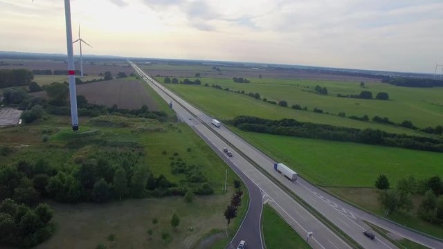 Road with car truck lorries moving both directions and wind turbine mills aerial 4k. Fly above highway traffic in Germany countryside green field plain. Logistics goods delivery vehicles in Europe