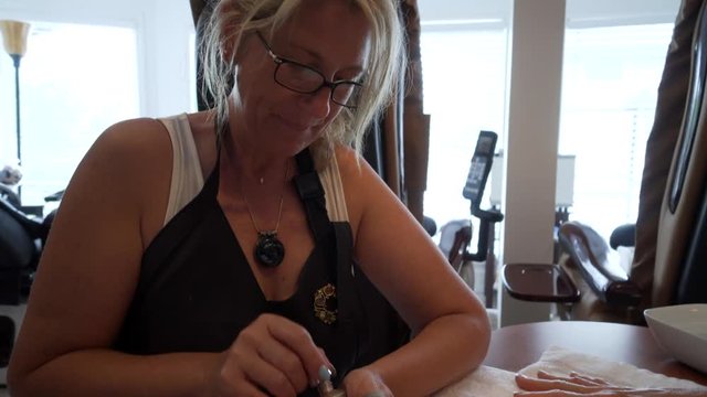Tight shot of a manicurist applying polish to nails of a white woman.  Camera angles up to end on face of blonde manicurist.