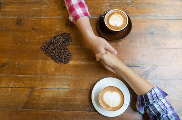 Coffee cups and holding hands at the wooden table