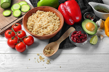 Composition with cooked quinoa and fresh vegetables on white wooden background