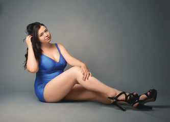 Beautiful overweight woman in blue swimsuit on grey background