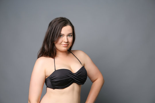 Beautiful overweight woman in black bikini on grey background