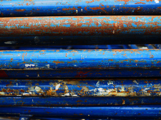 Old rusty dirty damaged peeled off blue painted iron steel construction rod stacking horizontally, close up shot