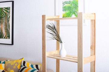 Branch with tropical leaves on wooden shelf in living room