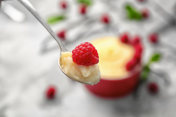Teaspoon with vanilla pudding and raspberry on blurred background