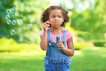 Cute African American girl blowing soap bubbles outdoors