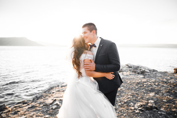 Wedding couple kissing and hugging on rocks near blue sea