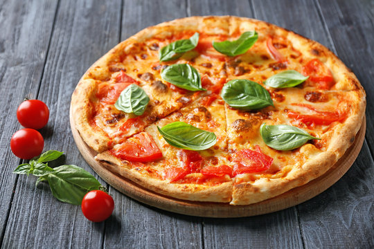Delicious pizza with cherry tomatoes and fresh basil on kitchen table