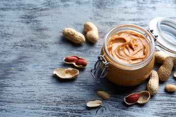 Glass jar with peanut butter on wooden background