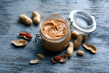 Glass jar with peanut butter on wooden background