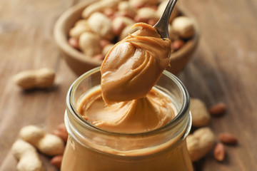 Spoon and glass jar with creamy peanut butter on kitchen table, closeup - obrazy, fototapety, plakaty