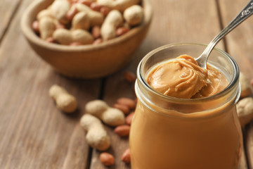 Spoon and glass jar with creamy peanut butter on kitchen table, closeup
