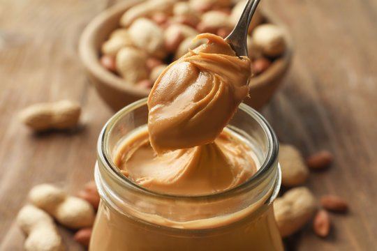 Spoon and glass jar with creamy peanut butter on kitchen table, closeup