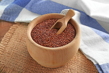 Red quinoa and wooden scoop in bowl on sackcloth