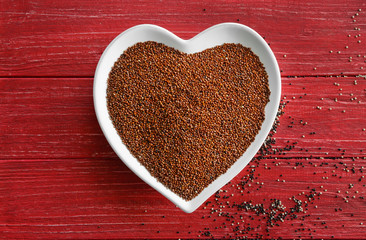 Red quinoa in heart shaped plate on wooden background