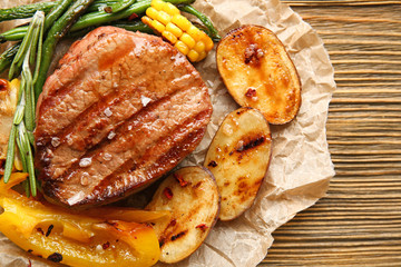 Composition with delicious grilled steak and vegetables on wooden table