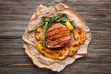 Composition with delicious grilled steak and vegetables on wooden table