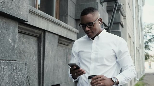 African american man using app on smart phone in city. Handsome young businessman using smartphone, scrolling pictures phone. Smiling and happy. Male using wireless earphones. Surfing internet