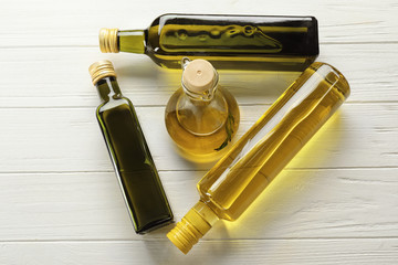 Bottles with different cooking oil on light wooden background