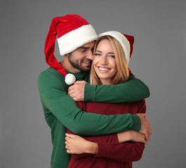 Happy young couple in Santa hats on grey background. Christmas concept