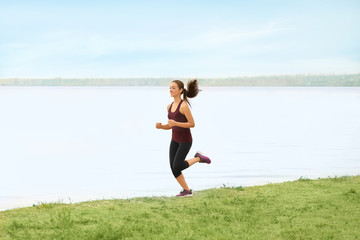 Young sporty woman running on river shore