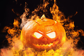 Closeup jack-o-lantern Halloween pumpkin with fire burning around at dark background.
