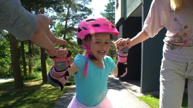 First skating. Parents Help Their Little Daughter to Skate on Roller Skates. Slow Motion.