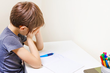 Naklejka premium Little kid made his homework at home. The boy is tired and covers his face with hands