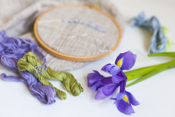 Вышивка с пастельных тонах нитками мулине на  деревянных пяльцах, на льняной ткани, фиолетовые, зеленые и голубые нитки  и цветок ириса
