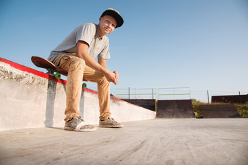 A teenage boy is sitting on a skateboard in the park and smiling