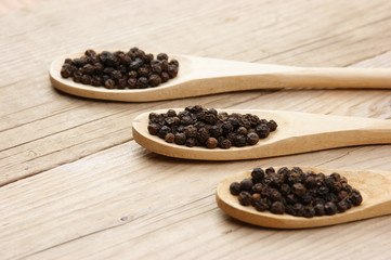 Black pepper in wooden spoon on the old board