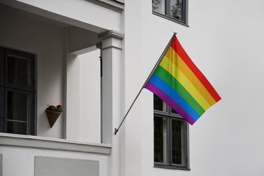 Rainbow Flag. LGBT (Lesbian, Gay, Bisexual, Transgender) Movement Flag Displaying On A Pole In Front Of The House And Waving On A Home, Hanging From A Pole On A Front Door Of A Building.