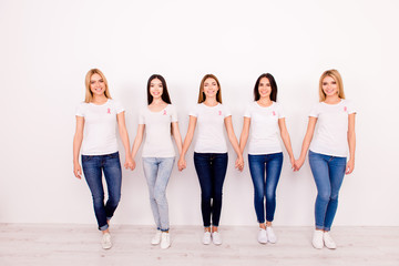 Obraz premium Life after fighting breast cancer exist. Carefree, international, cured, cheerful five girls are holding each other`s arms, walking to new life together, with pink ribbons symbols on chest