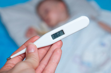 the hand holds a thermometer with 38.2 degrees Celsius on the background of the child sleeping in bed
