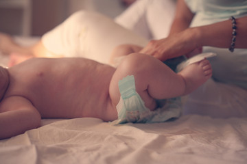 Mother with her baby at home. Mother changing diaper her little baby on the bed.
