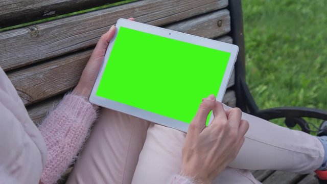 Young Woman in pink jeans sitting on bench uses Tablet PC with pre-keyed green screen. Few types of gestures - scrolling up and down, tapping, zoom in and out. Perfect for screen compositing