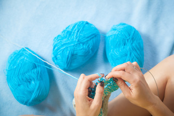 close-up of a young woman pulling a thread and knitting with knitting needles from natural mohair...
