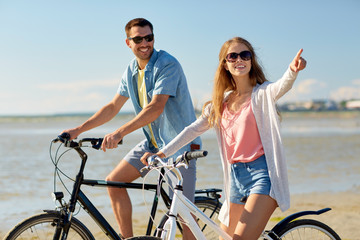 happy young couple riding bicycles at seaside