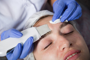 Fototapeta premium A close-up of the beautician makes a face cleaning in blue medical gloves to a girl with a problem skin, an outgoing facial treatment for cleansing the skin