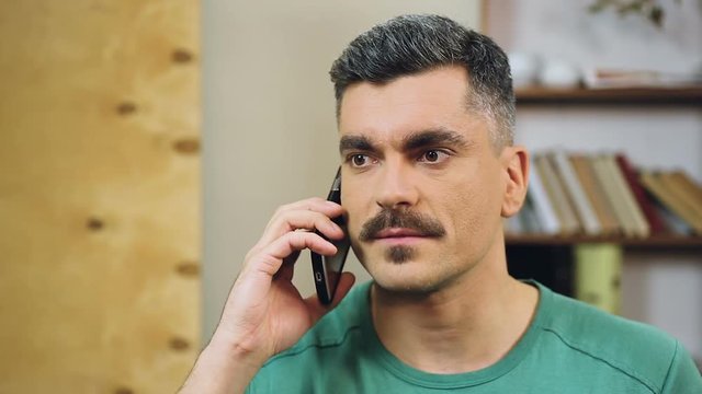 Gray-haired man talking on cellphone at home, making appointment with friends