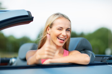 happy young woman in convertible car thumbs up