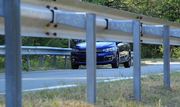 Highway railings fenced asphalt road and blue sedan on the road
