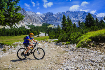 Fototapeta premium Tourist cycling in Cortina d'Ampezzo, stunning rocky mountains on the background. Woman riding MTB enduro flow trail. South Tyrol province of Italy, Dolomites.