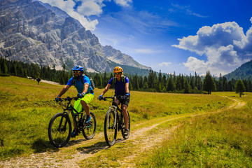 Obraz premium Tourists cycling in Cortina d'Ampezzo, stunning rocky mountains on the background. Man riding MTB enduro flow trail. South Tyrol province of Italy, Dolomites.