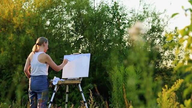 The girl with enthusiasm draws paints on a paper a landscape
