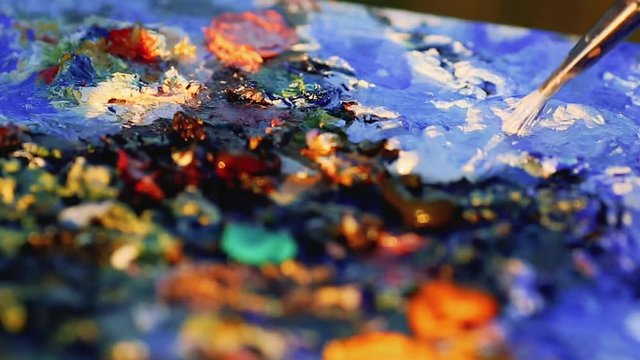 Artist brush mix color oil painting on palette is holding in his hand closeup